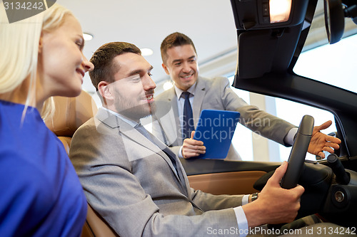 Image of happy couple with car dealer in auto show or salon