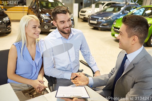 Image of happy couple with car dealer in auto show or salon