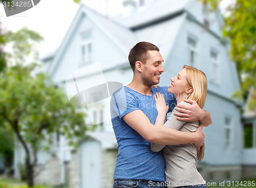 Image of smiling couple hugging over house background