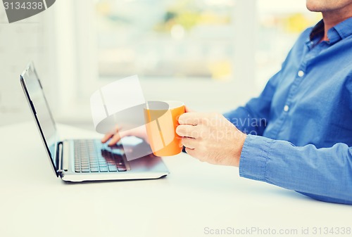 Image of male hand with cup of tea or coffee and laptop