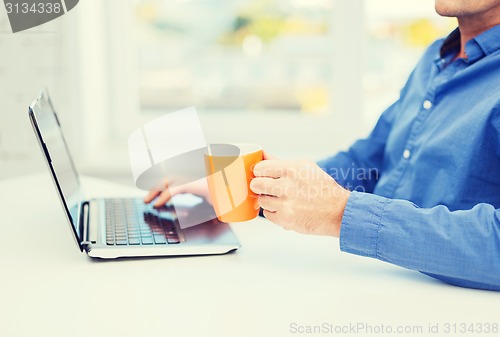 Image of male hand with cup of tea or coffee and laptop