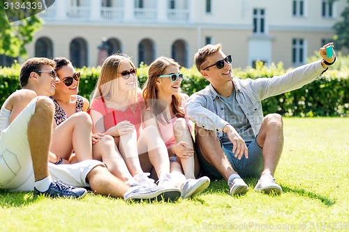 Image of smiling friends with smartphone sitting on grass
