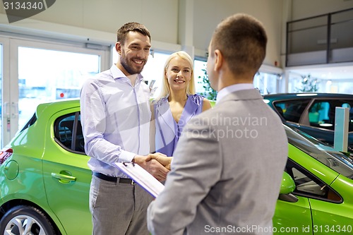 Image of happy couple with car dealer in auto show or salon