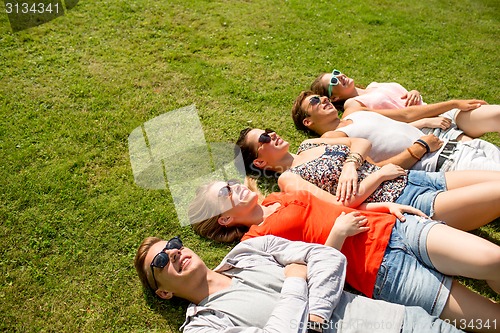 Image of group of smiling friends lying on grass outdoors