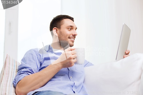 Image of smiling man with tablet pc and cup at home