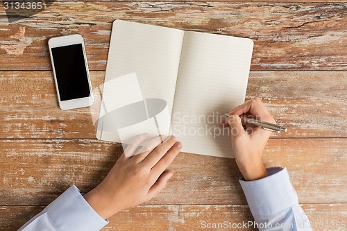 Image of close up of hands with notebook and smartphone