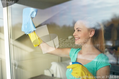 Image of happy woman in gloves cleaning window with rag