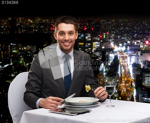 Image of smiling man with tablet pc eating main course