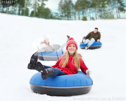 Image of group of happy friends sliding down on snow tubes