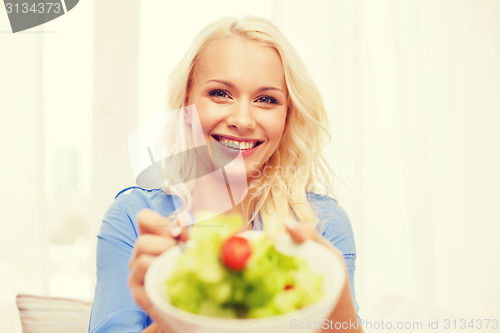 Image of smiling young woman with green salad at home