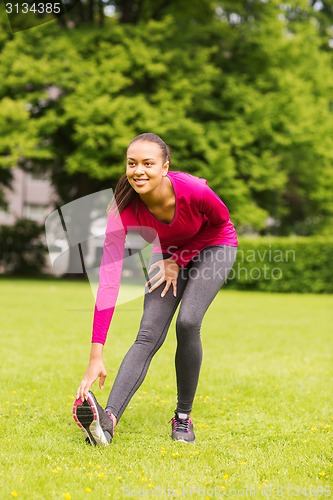 Image of smiling black woman stretching leg outdoors