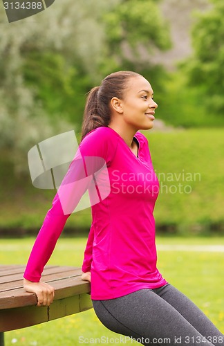 Image of smiling woman doing push-ups on bench outdoors