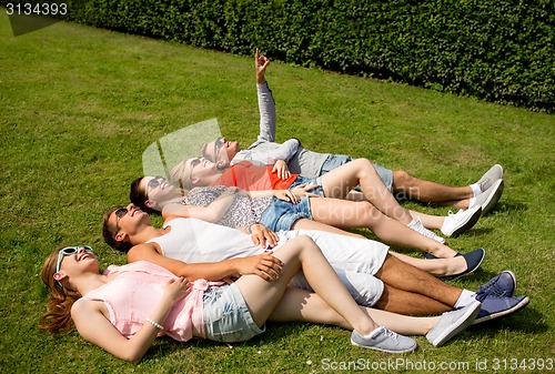 Image of group of smiling friends lying on grass outdoors