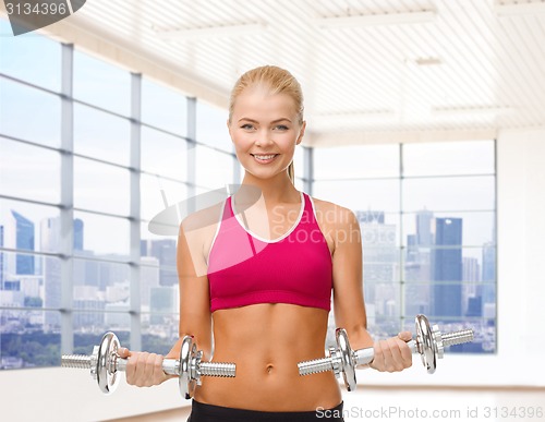 Image of smiling woman with dumbbells flexing biceps in gym