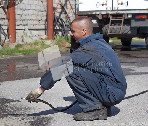 Image of Worker in overalls watering area with water 