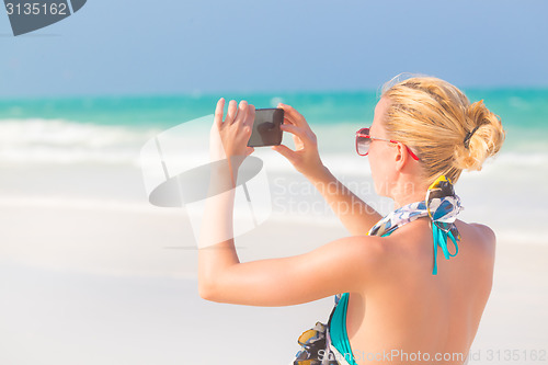 Image of Woman taking photo on the beach.