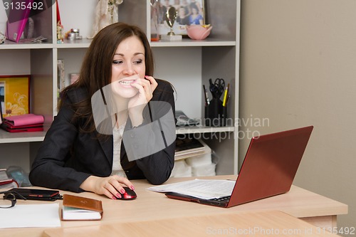 Image of Nervous girl in office bites his nails, working on computer