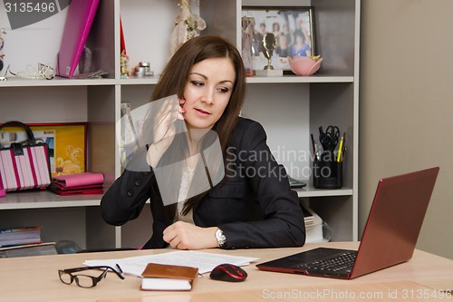 Image of Business woman in office talking on phone looking at monitor