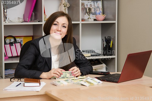 Image of Office worker sitting at table with a bunch of money and looks in picture