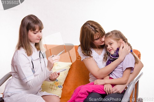 Image of doctor looks temperature on a thermometer sick girl and her mother comforts