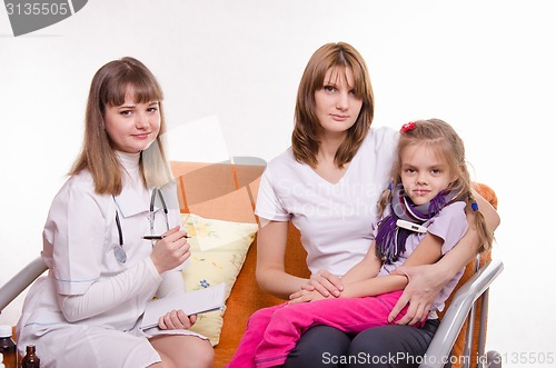 Image of Sick girl measures the temperature of sitting on lap mother and doctor writes a complaint