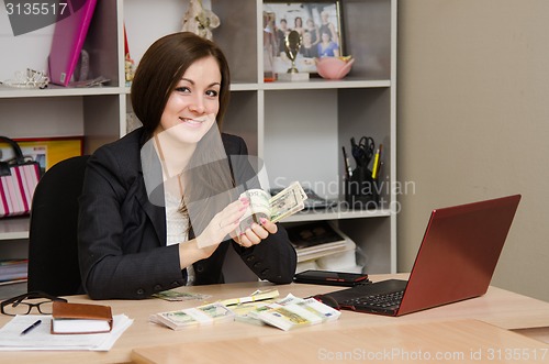 Image of Girl in office happily turns the money a pack