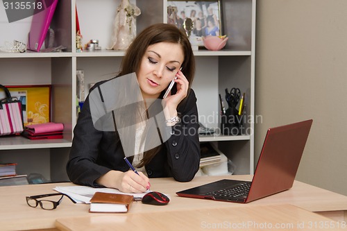 Image of Business woman in office talking on phone and writes table