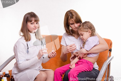 Image of Pediatrician is going to get a shot sick child sitting on hands of mother