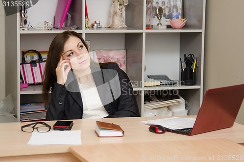 Image of Thoughtful girl in the office sitting at a table computer and relies head on her hand