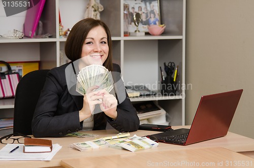 Image of girl behind desk office in front him holding a fan of money