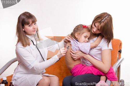 Image of Children's doctor listening to breathing girl sitting in hands of mother