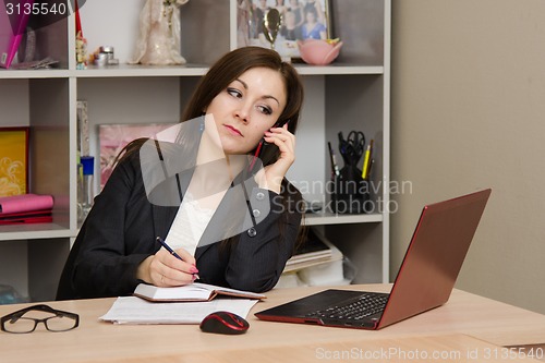 Image of girl at desk prepared to write in a notebook information obtained from telephone conversation