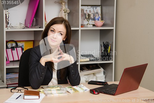 Image of Head girl sitting at a desk with pile money her hands folded in front of him