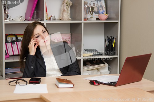 Image of girl in office sitting a table at computer and relies head on her hand