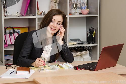 Image of Business woman talks by phone and counts money