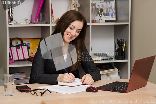 Image of Female office worker grinning writing in a notebook for your desktop