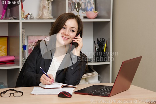 Image of Business woman talking on phone and writes in a diary