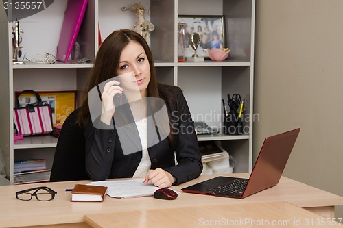 Image of employee of the office sitting a table holding phone and looking at frame