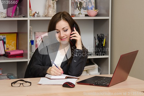 Image of Business woman writing in a notebook and talking on phone