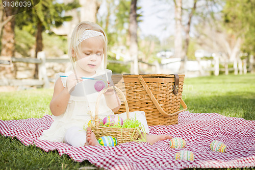 Image of Cute Baby Girl Coloring Easter Eggs on Picnic Blanket