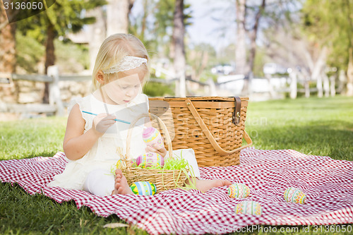 Image of Cute Baby Girl Coloring Easter Eggs on Picnic Blanket