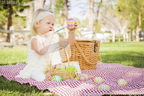 Image of Cute Baby Girl Coloring Easter Eggs on Picnic Blanket