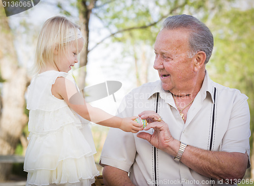 Image of Cute Baby Girl Handing Easter Egg to Grandfather Outside