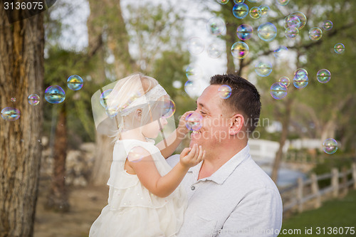 Image of Father Holding Baby Girl Enjoying Bubbles Outside at Park