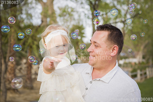 Image of Father Holding Baby Girl Enjoying Bubbles Outside at Park