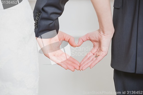 Image of wedding couple showing shape of heart from their hands.