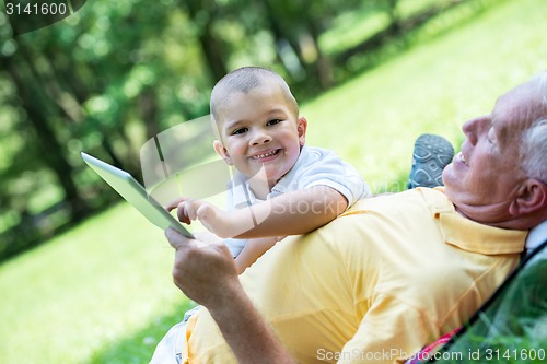 Image of grandfather and child in park using tablet