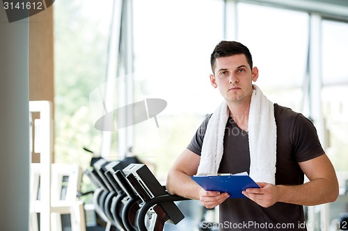 Image of trainer with clipboard standing in a bright gym