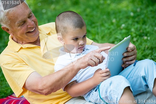 Image of grandfather and child in park using tablet