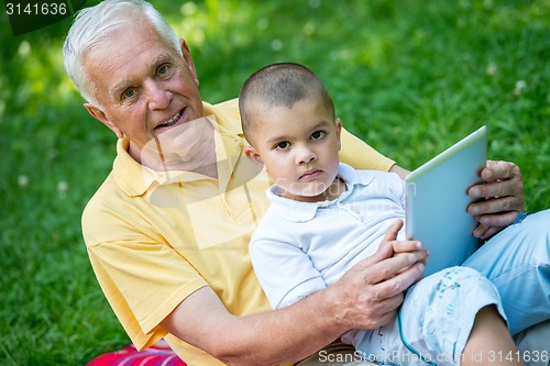 Image of grandfather and child in park using tablet